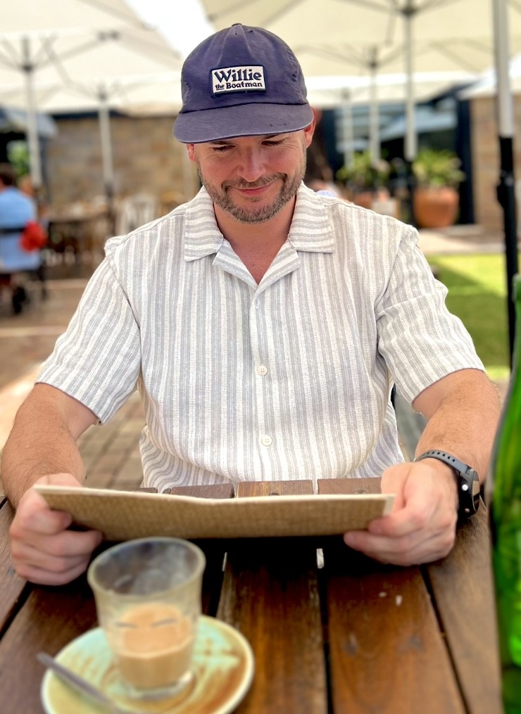 Seb, founder of Under the Flight Path, reading a menu at a cafe